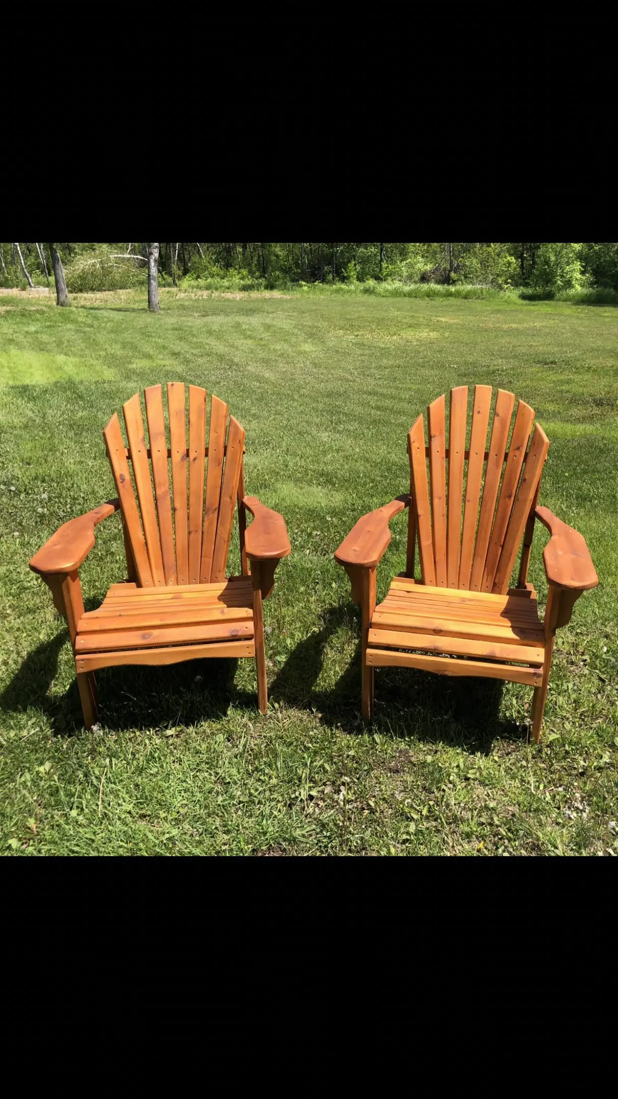 Two wooden Adirondack chairs on green grass in sunlight.