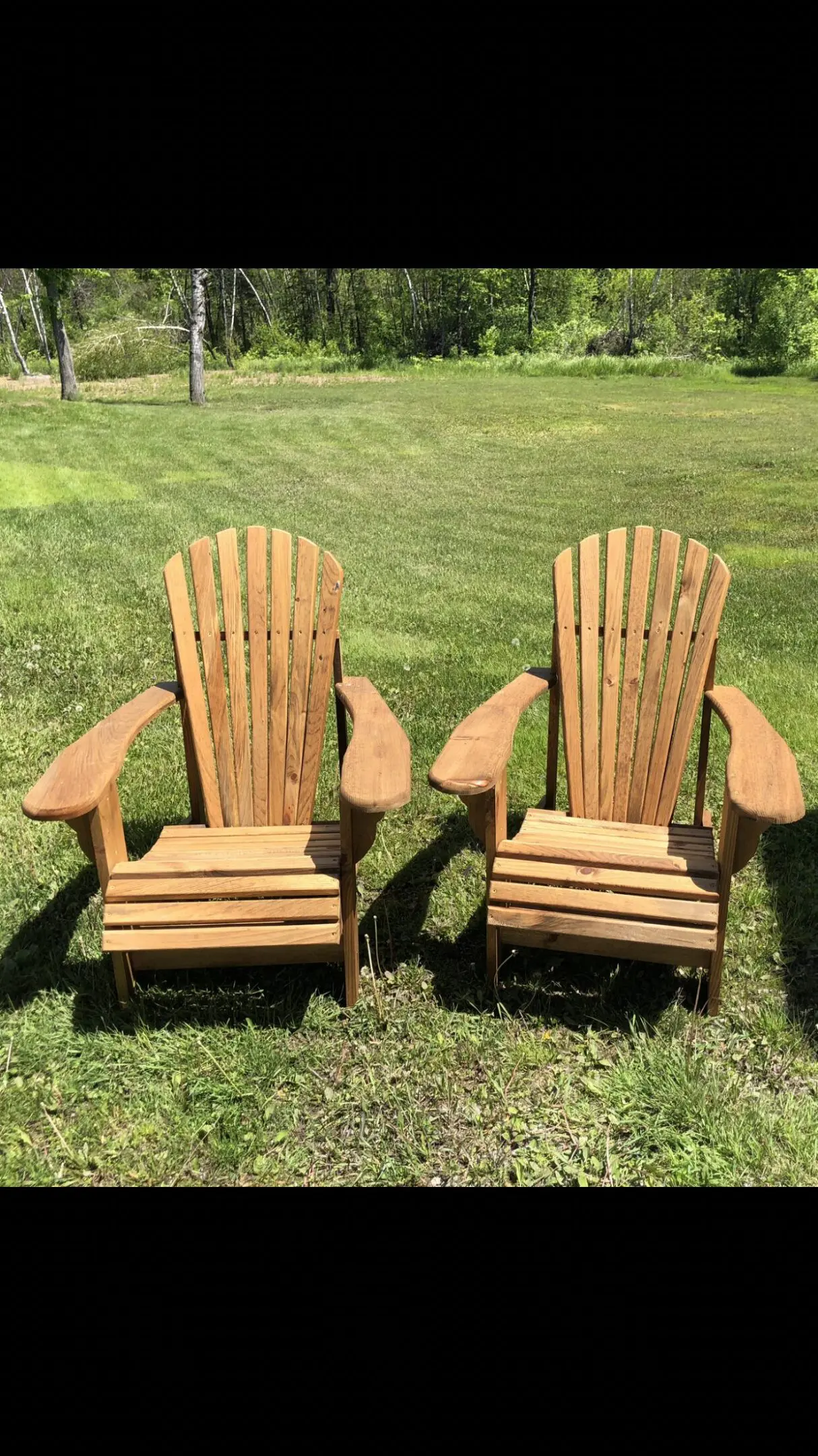 Two wooden Adirondack chairs on green grass in a sunny garden.