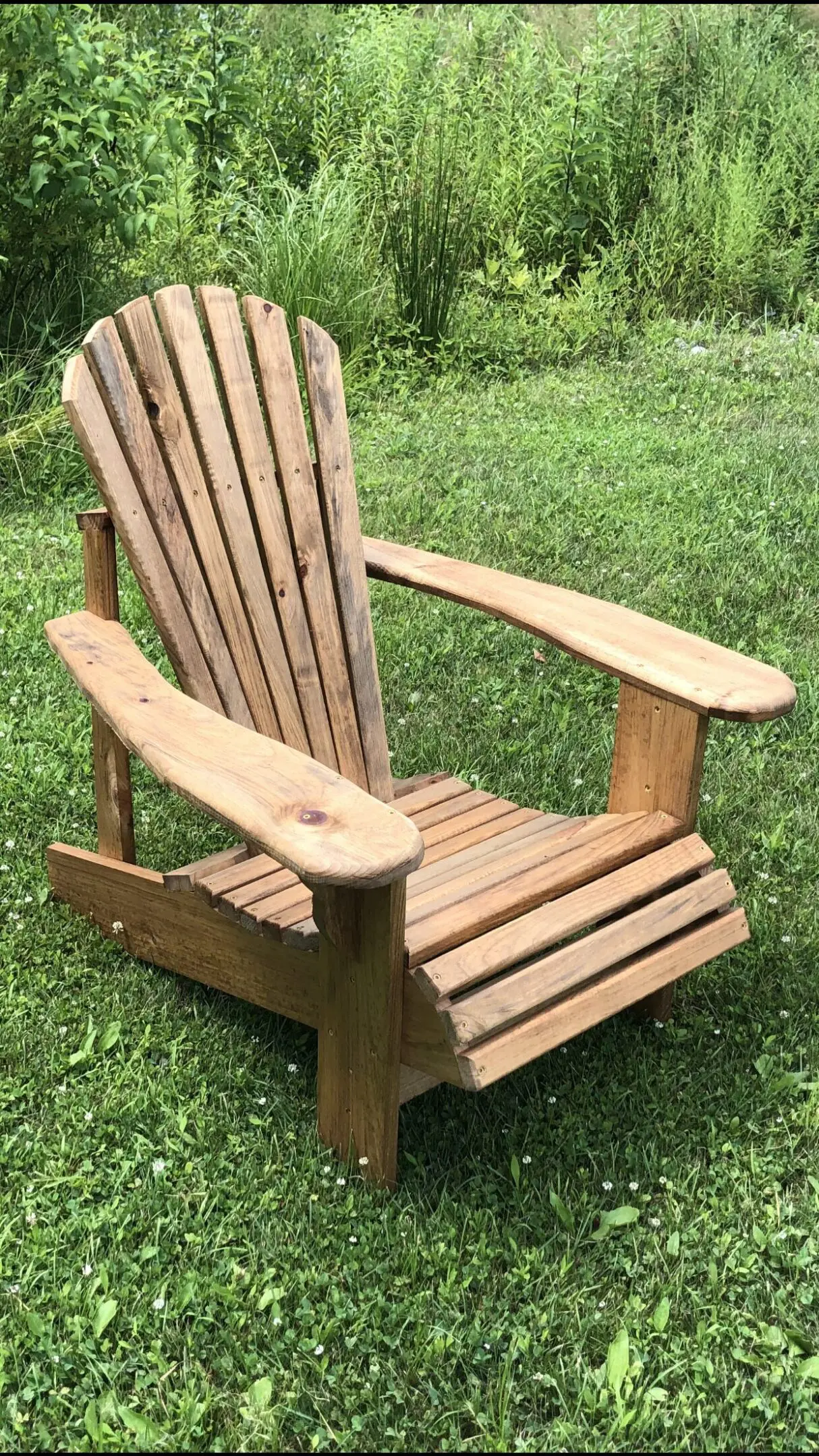 Wooden Adirondack chair on green grass outdoors.