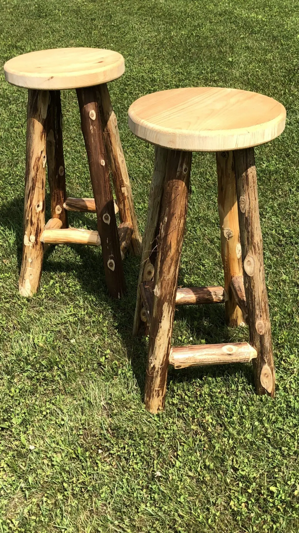 Rustic wooden stools with natural bark finish on green grass.