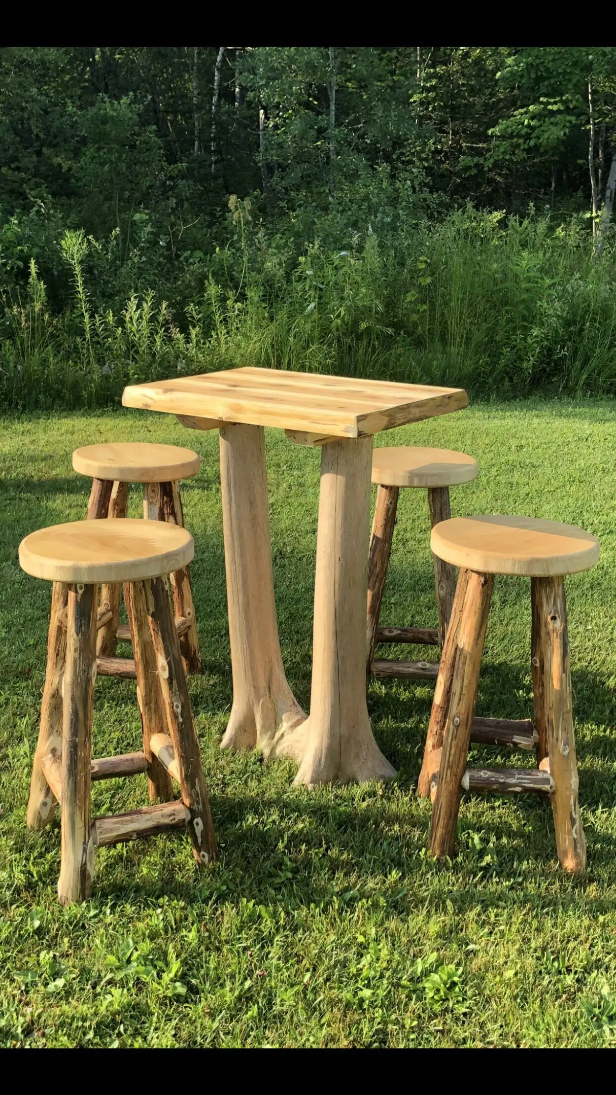 Rustic wooden outdoor table with four matching stools on grass.