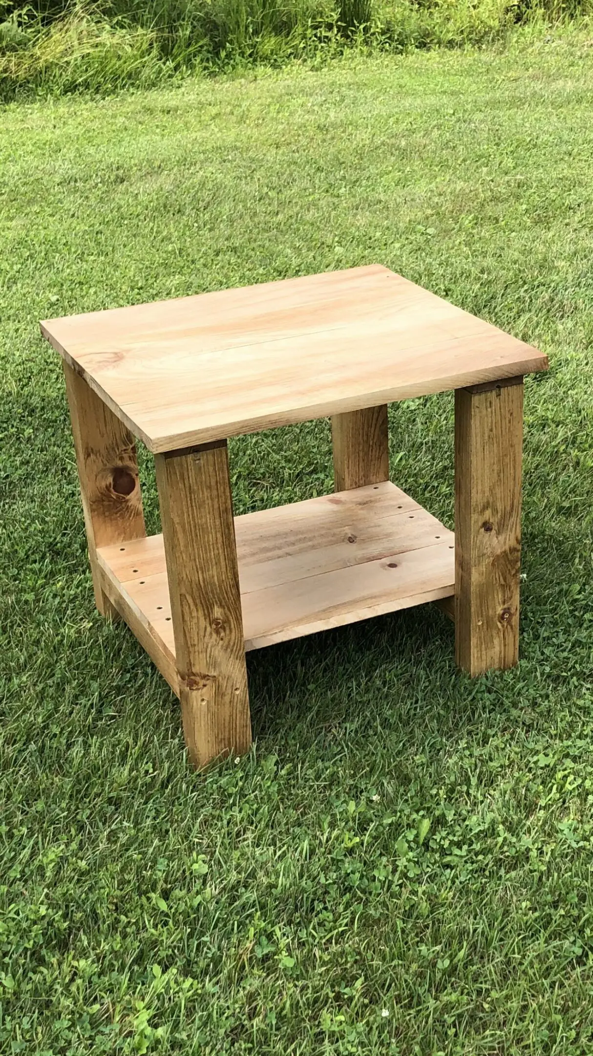 A rustic wooden side table with a lower shelf on grass.