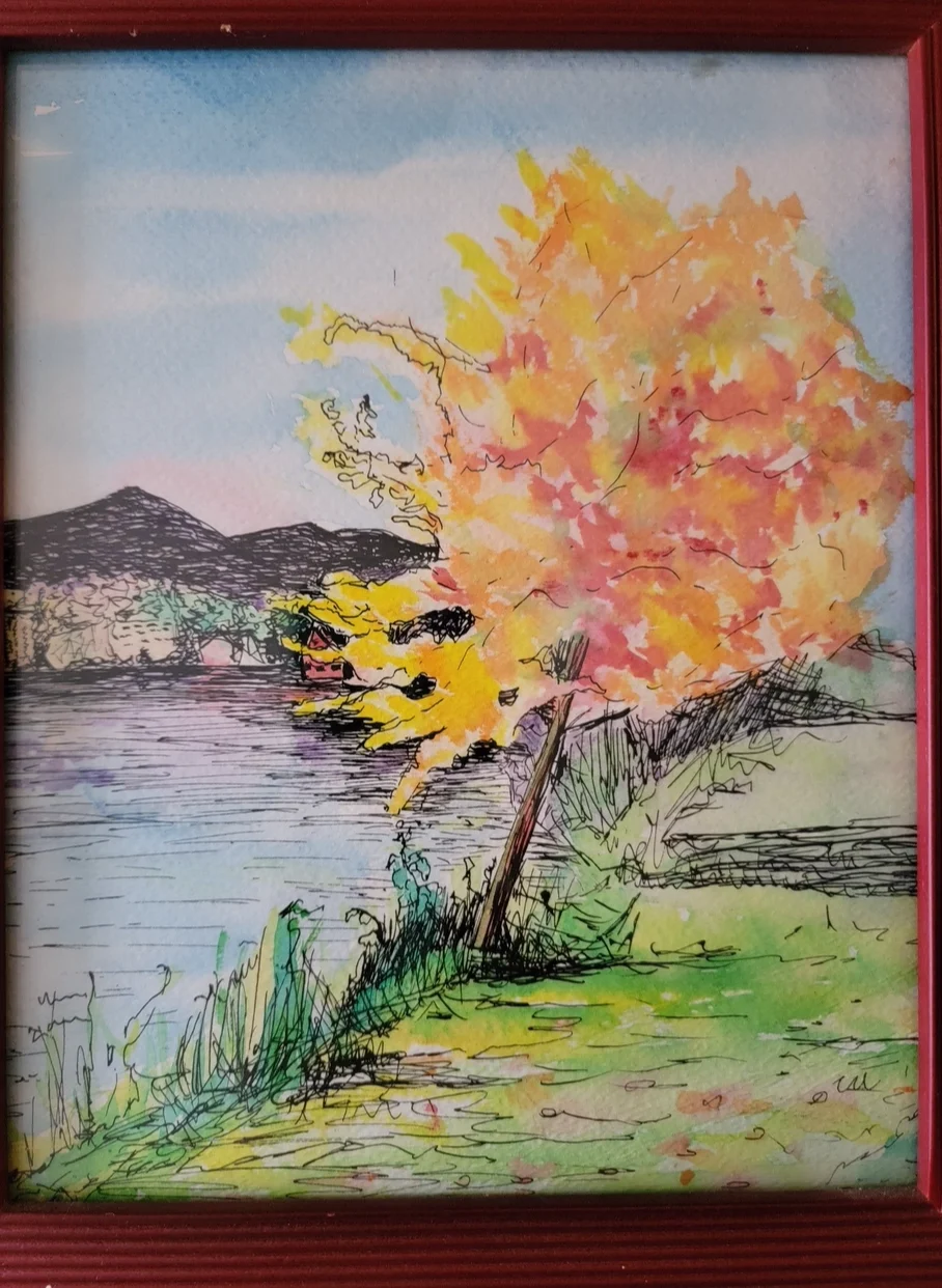 A vibrant autumn tree by a lakeside with mountains in the background.