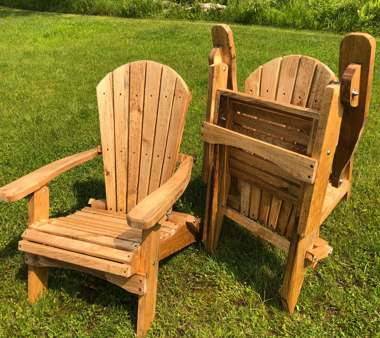 Wooden Adirondack chairs on a grassy lawn in sunlight.